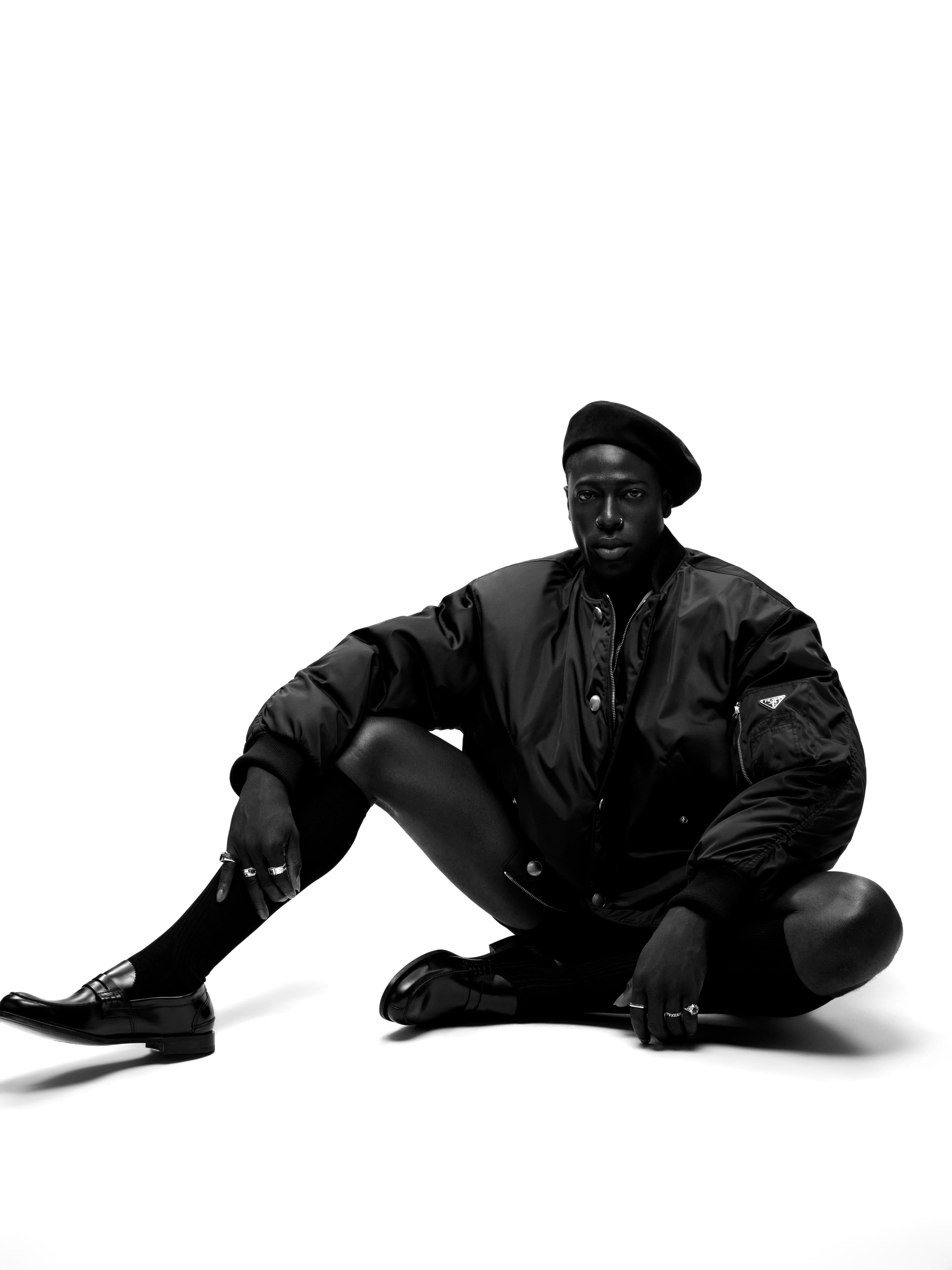 JACKET by ,Prada,. TOP and SHORTS by ,Merz b. Schwanen,. HAT, stylist’s own. SOCKS by ,Falke,. SHOES by ,Church’s,. RINGS by ,HOWL,, ,Mateo,, and ,Miansai,, and Sumney’s own.