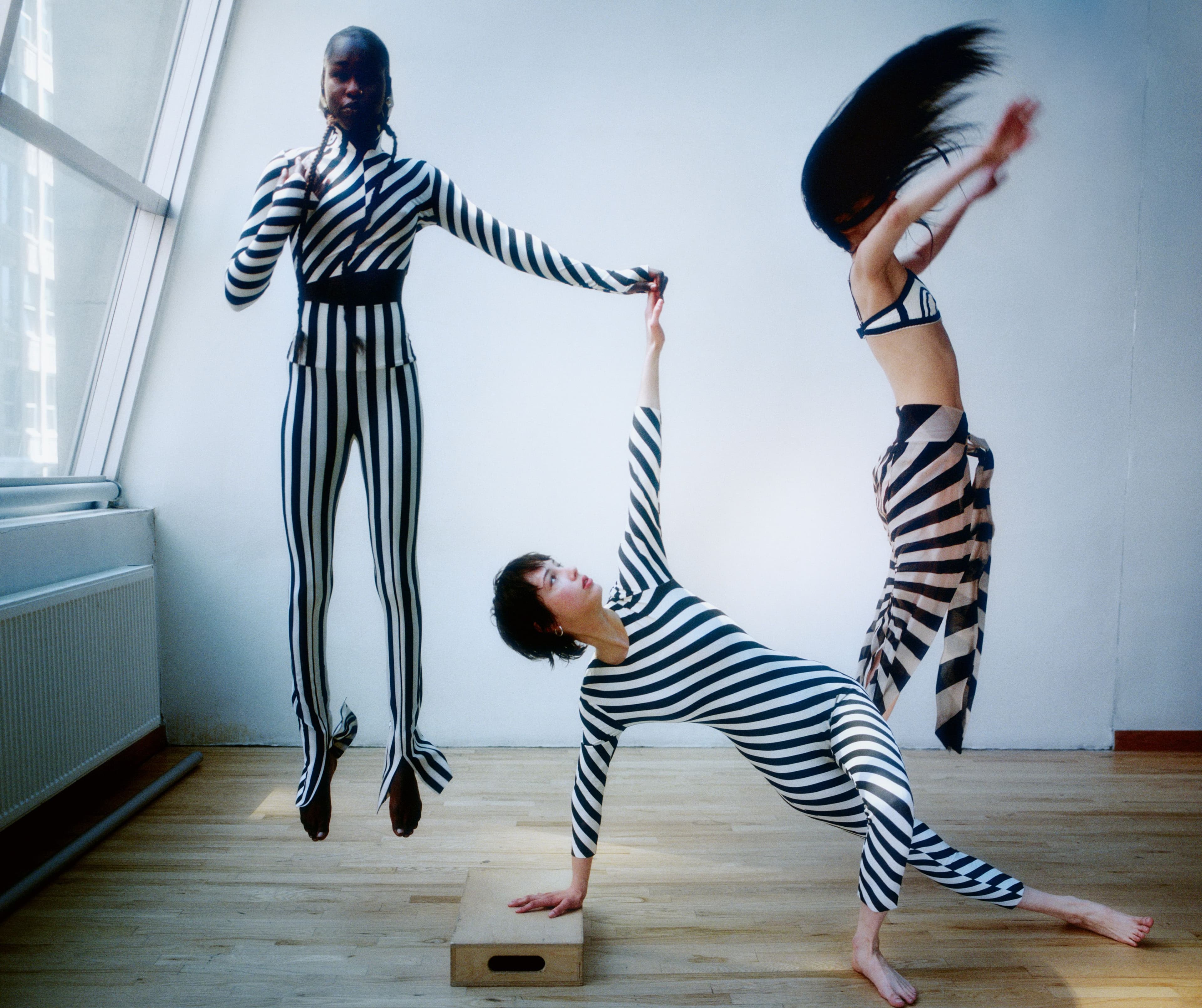 From left: Noi Dwol wears all clothing by Norma Kamali. Earrings by Ariana Boussard-Reifel. Johnson wears bodysuit by Norma Kamali. Earrings by Santangelo. Yulu wears bra by Helmut Lang. Vintage skirt by Gareth Pugh from the Albright Fashion Library. Earrings by Britt Bolton. Anklet by Santangelo.